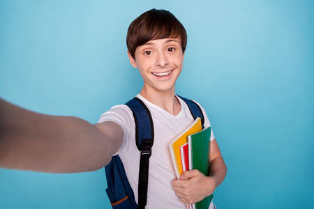 Photo of glad nice school boy photographing himself on his way to school while isolated with blue backgroundの写真素材