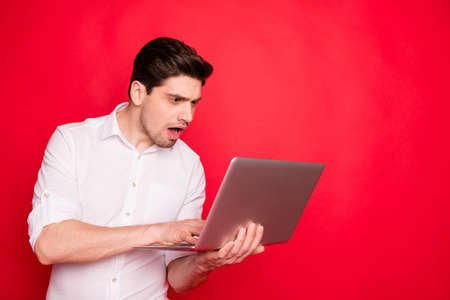 Photo of frightened man, wearing white shirt seeing no money on his accounts on screen of laptop while isolated with red backgroundの写真素材