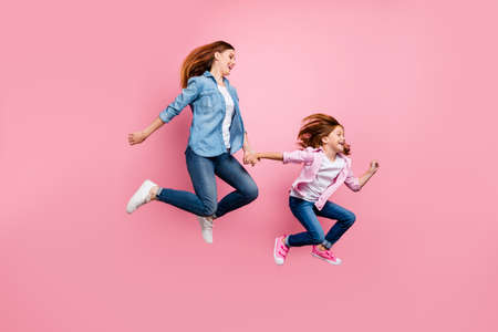 Foxy small lady and her mom jumping high rushing toy shop wear casual jeans outfit isolated pink backgroundの写真素材