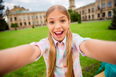 Close up photo of cheerful kid with pigtails screaming laughing making photo wearing checkered...