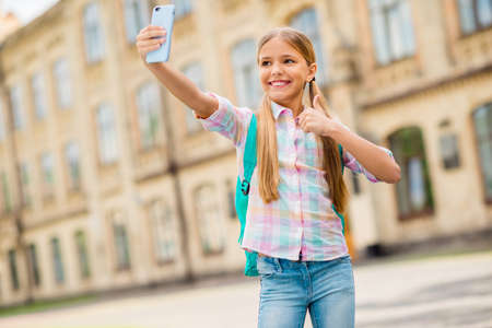 Portrait of pretty kid with pigtails ponytails making photo approve college wearing checkered plaid t-shirt denim jeans standing outdoorsの写真素材