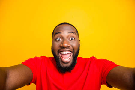 Self portrait of rejoicing overjoyed black man playing new camera with face delighted while isolated with yellow backgroundの写真素材