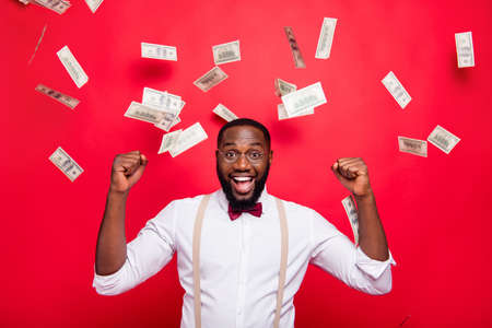 Overjoyed dark skin guy rejoicing money rain dressed formal wear isolated red backgroundの写真素材