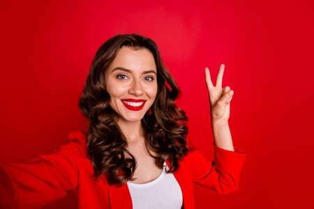 Close up photo of stunning girl making v-sign take selfie wearing jacket isolated over red...