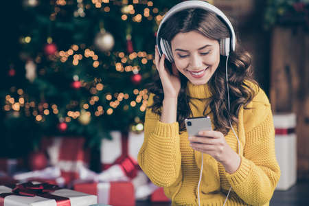Photo of charming beautiful wavy curly haired girl listening to music wearing yellow pullover...