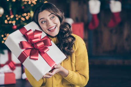 Close up photo of cute nice charming beautiful attractive girlfriend listening to what is inside box wearing jeans denim yellow pulloverの写真素材