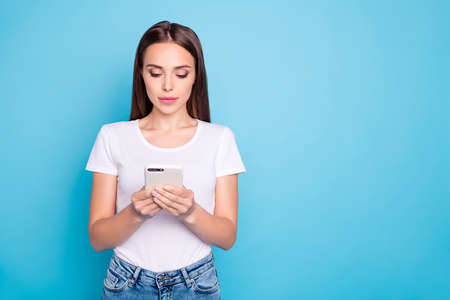 Portrait of concentrated youth holding device reading news wearing white t-shirt denim jeans...