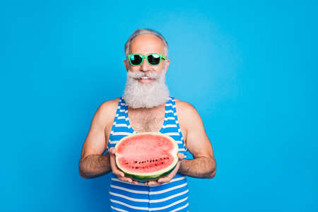 Portrait of cheerful man with eyeglasses eyewear holding watermelon wearing striped swim wear isolated over blue backgroundの写真素材