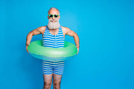 Portrait of cheerful man with eyeglasses eyewear holding rubber ring life belt wearing swim wear isolated over blue backgroundの写真素材