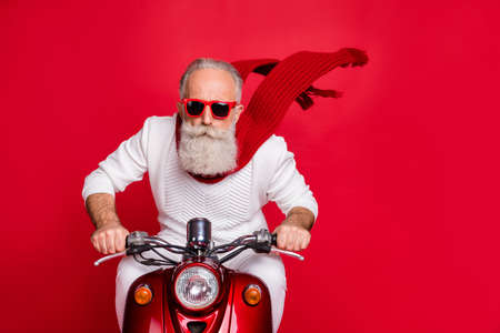 Close up photo of cool pensioner riding his bike with air wind blowing wearing white jumper sweater isolated over red backgroundの写真素材
