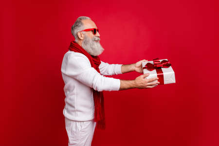 Aged hipster man giving big giftbox to grandchild wear sun specs knitted jumper isolated red...