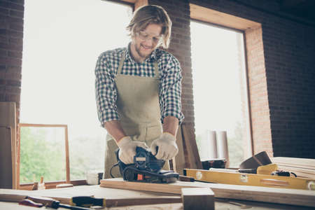 Photo of handsome foreman, guy making furniture using grinder and sandpaper in carpentryの写真素材