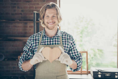 Portrait of his he nice attractive, handsome cheerful cheery guy woodworker holding in hands creative accessory decor heart shape 14 February at industrial brick loft style interior workplaceの写真素材