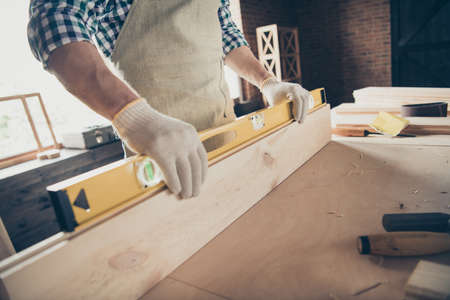 Cropped profile side view of his he, nice skilled guy woodworker holding in hands instrument checking surface long board at industrial brick loft style interior indoorsの写真素材