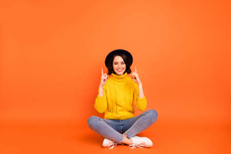 Photo of excited cheerful funny girl pointing up wearing jeans denim headwear cap while isolated with orange backgroundの写真素材