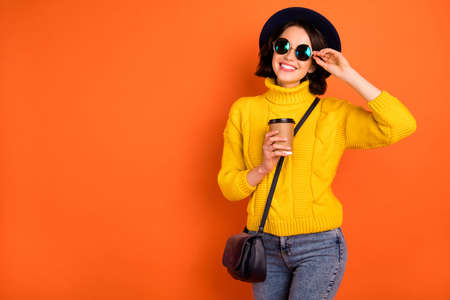 Photo of relaxing chilling girlfriend wearing cap enjoying her vacation with coffee cup while isolated with orange backgroundの写真素材