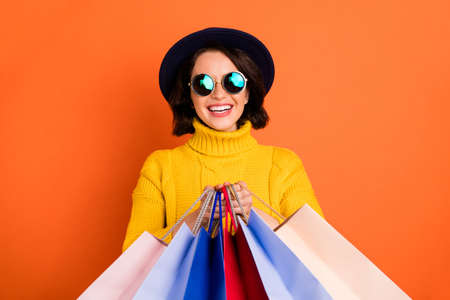 Photo of shopping cheerful girl wearing cap showing you what she has bought while isolated with...