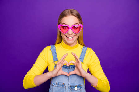 Portrait of cheerful lady making heart symbol with her fingers wearing yellow turtleneck having eyewear eyeglasses isolated over purple violet backgroundの写真素材