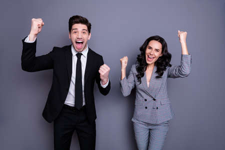 Portrait of ecstatic business people with wavy curly brunette hair raising fists screaming yeah wearing black blazer jacket trousers tuxedo pants isolated over gray backgroundの写真素材