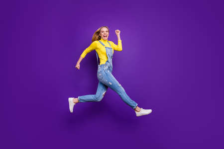 Full length photo of cheerful teenager running screaming wearing yellow turtleneck denim jeans overalls isolated over violet purple backgroundの写真素材