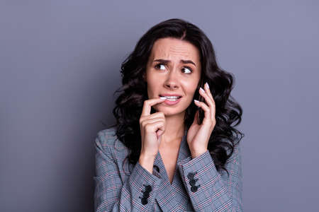 Close up photo of frustrated collar with wavy curly hair nail biting having fearful dialogue wearing stylish jacket blazer isolated over grey backgroundの写真素材