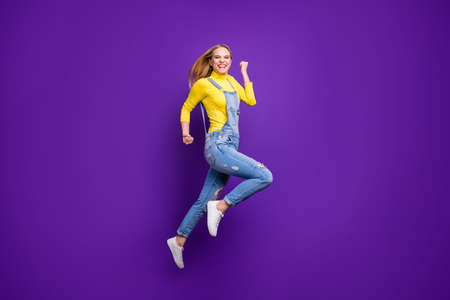 Full size photo of cheerful girl raising her fists screaming yeah wearing yellow turtleneck denim jeans isolated over purple violet backgroundの写真素材