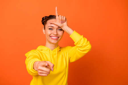 Portrait of childish person, directing mocking wearing yellow hood sweater isolated over orange...