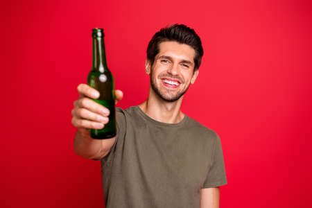 Photo of amazing guy with green beer ale bottle spending great time wear casual grey t-shirt isolated on red backgroundの写真素材
