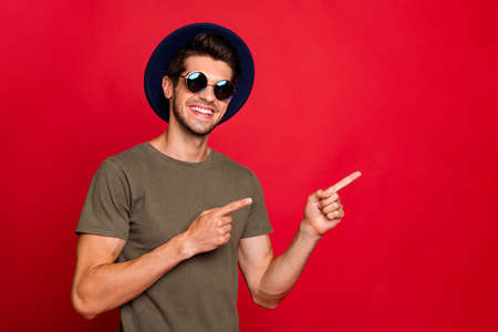 Photo of macho guy indicating fingers empty space wear vintage hat sun specs and grey t-shirt isolated on red backgroundの写真素材