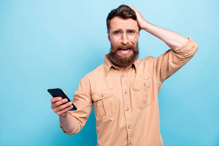 Portrait of frustrated man touching his head screaming wearing eyeglasses eyewear brown shirt isolated over blue backgroundの写真素材