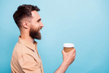 Profile side photo of one guy holding cup smiling wearing brown shirt isolated over blue background