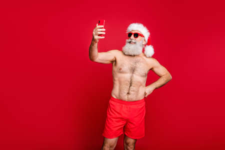 Portrait of his he nice attractive handsome funky cheerful cheery bearded gray-haired man wearing trunks taking making selfie weekend isolated over bright vivid shine red backgroundの写真素材