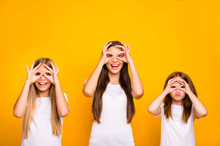 Funny three sister ladies holding hands in okey symbols near eyes like specs wear casual outfit isolated yellow backgroundの写真素材