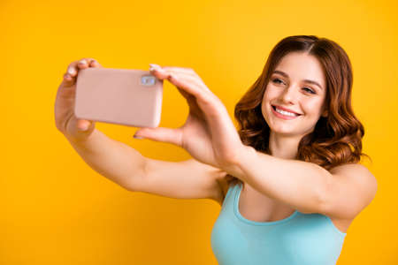 Photo of pretty lady holding telephone in hand making selfies wear tank-top isolated yellow backgroundの写真素材