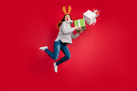 Nervous lady santa delivery service holding too much giftboxes wear head horns and knitted pullover isolated red backgroundの写真素材