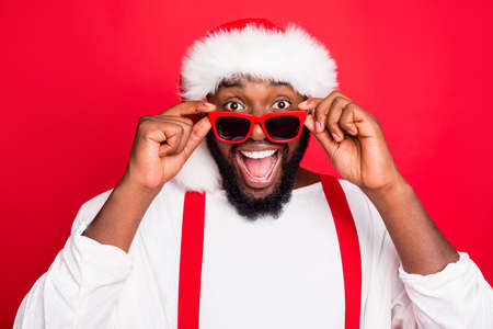 Close up photo of astonished african santa claus touching his specs screaming wow omg see noel miracle wearing stylish white sweater isolated over red backgroundの写真素材