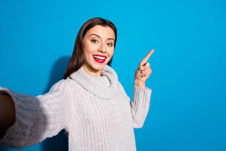 Photo of pretty lady making selfies indicating arm empty space wear warm knitted pullover isolated...