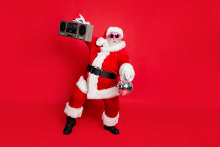 Full length photo of cute santa claus hold style sound boom box glittering ball dancing on noel party wear eyeglasses eyewear hat isolated over red backgroundの写真素材