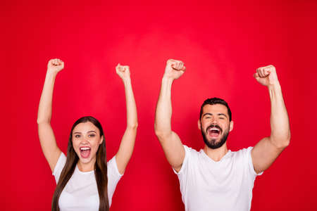 Photo of cheerful excited cute charming pretty couple of two people together rejoicing with victory of their favorite sport team wearing white t-shirt while isolated with red backgroundの写真素材
