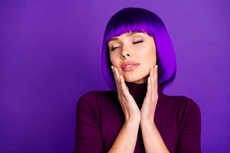 Close up photo of charming girl with her eyes closed touching cheeks wearing turtleneck isolated over violet purple backgroundの写真素材