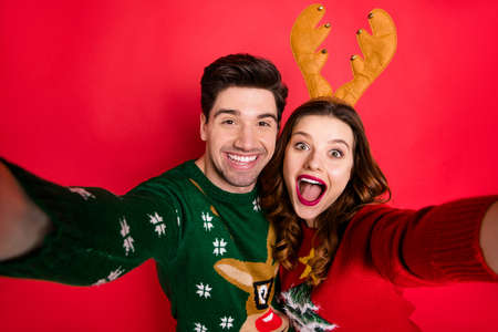 Photo of crazy lady and guy at x-mas costume party making selfies, wear knitted jumpers with ornament isolated red color backgroundの写真素材