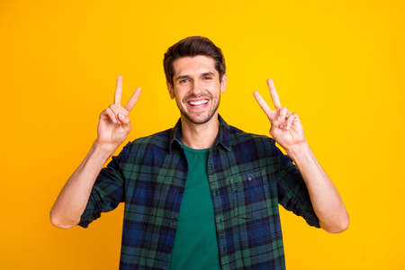 Close up photo of amazing macho guy showing v-sign symbols saying, hello to friends wear casual plaid shirt isolated yellow color backgroundの写真素材