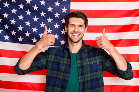 Photo of cool guy standing near usa flag exchange student raising thumbs up wear casual plaid shirt isolated on flag backgroundの写真素材