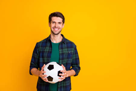 Photo of cool guy with white and black football ball excited to begin match wear casual plaid shirt isolated yellow color backgroundの写真素材