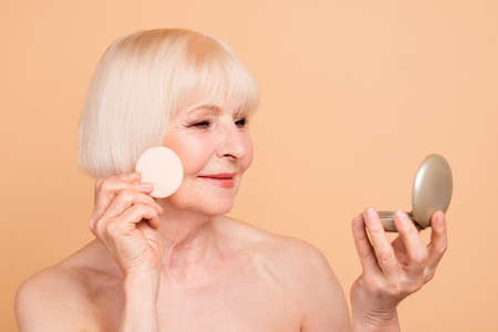 Close-up portrait of her she nice attractive well-groomed cheerful peaceful gray-haired lady looking at mirror beauty time isolated over beige backgroundの写真素材