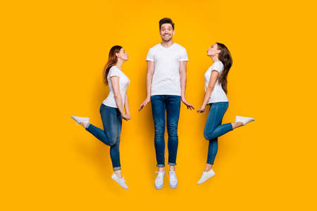 Full length body size view portrait of two nice attractive lovely lovable flirty cheerful cheery dreamy girls kissing one guy Valentine day isolated over bright vivid shine yellow backgroundの写真素材