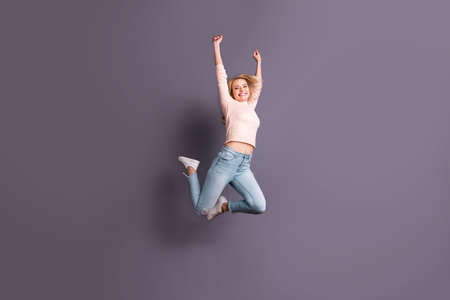 Full length photo of pretty lady jumping high competitive sporty mood raising hands up wear casual...