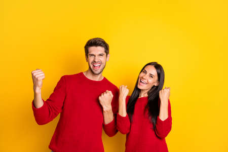 Portrait of cheerful two people raise fists scream yeah celebrate victory wear red pullover isolated over yellow backgroundの写真素材