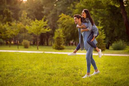 Full length profile side photo of lovely spouses piggyback wearing denim jeans jackets blazers outdoorsの写真素材