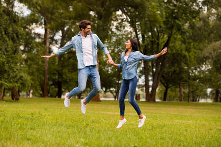 Full body photo of cute pair holding hands jumping high in green park wear denim outfitの写真素材